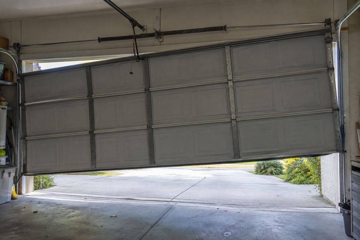 Garage door hanging crooked inside a garage, one side dropped out of its track