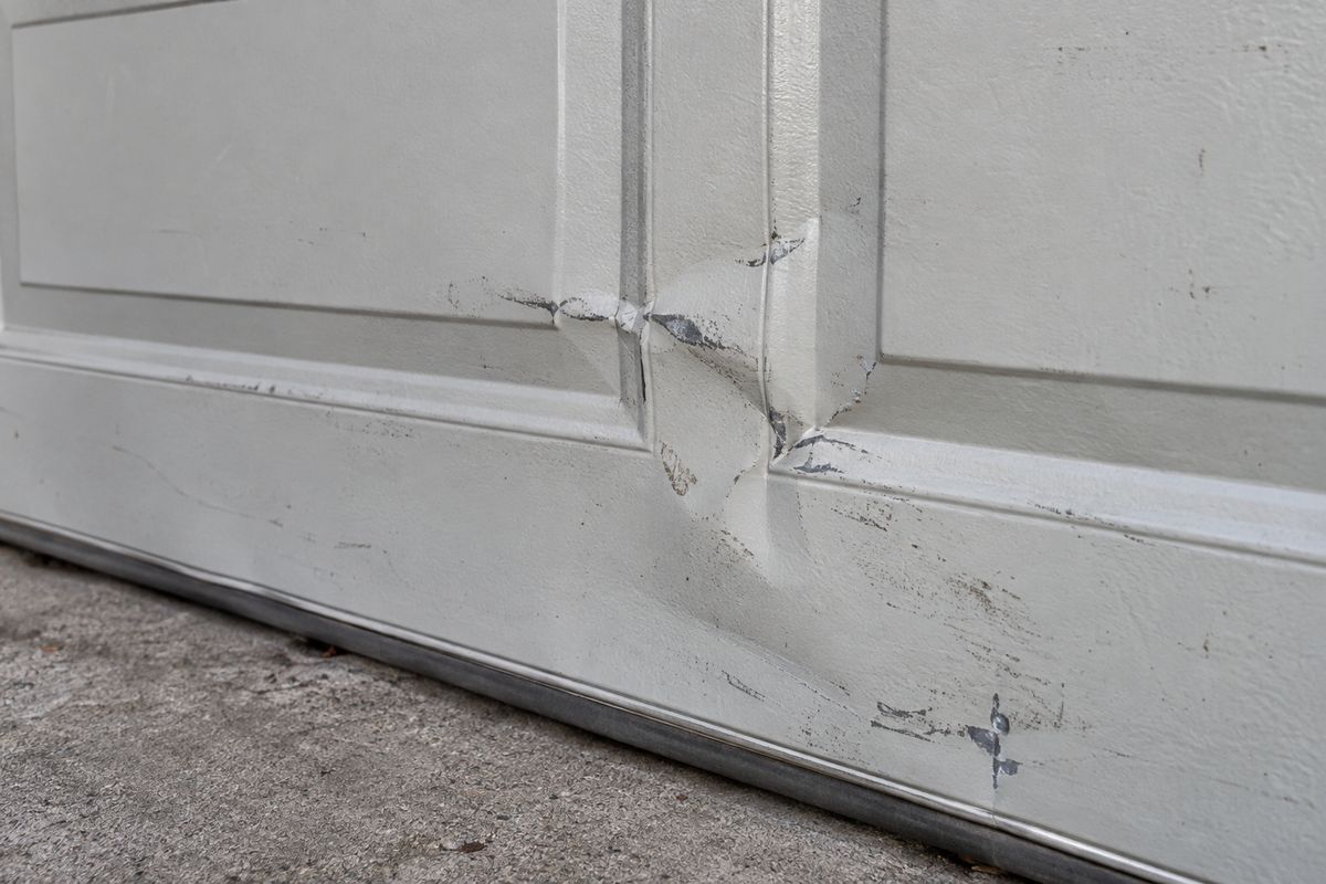 Creased, dented section of a white steel garage door with paint split along the crease