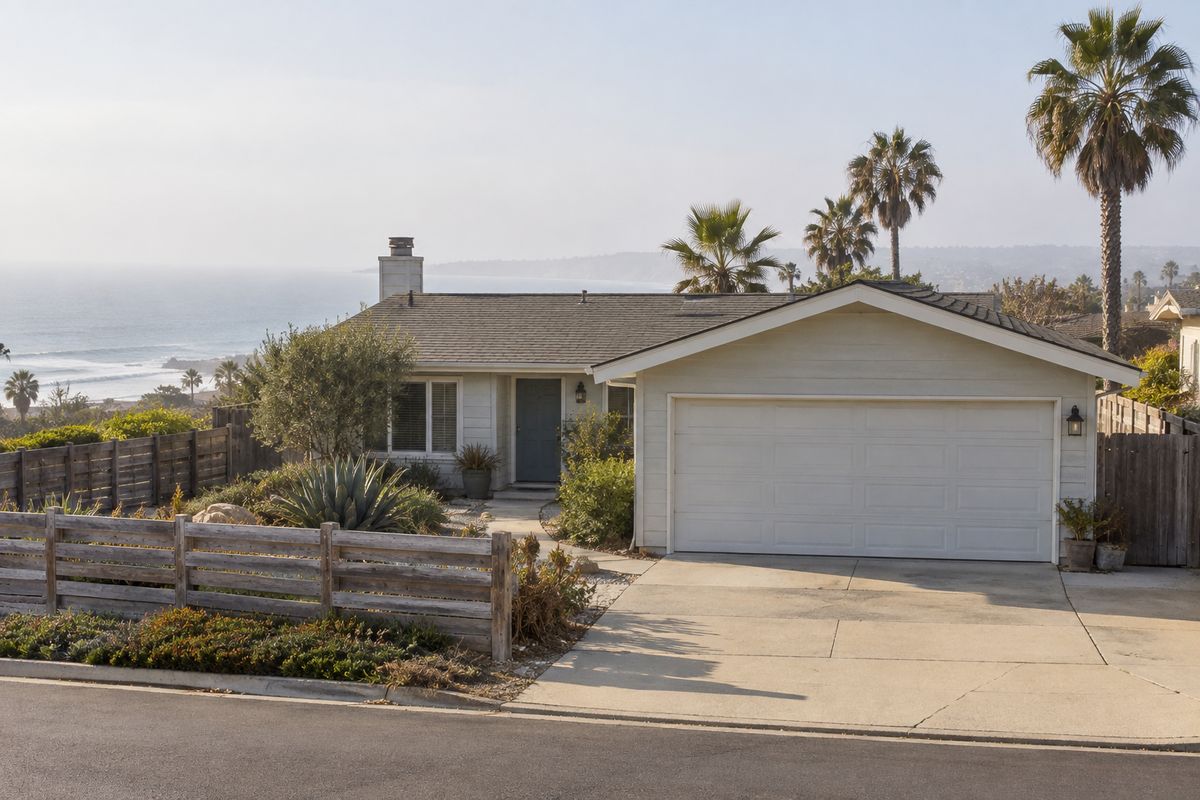Single-story coastal home with a white double garage door, palm trees and the ocean behind