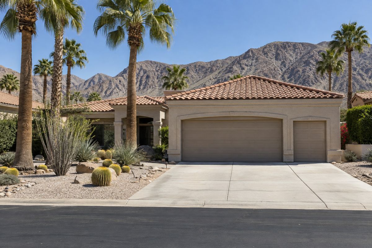 Desert home with a tile roof and garage doors, cactus planting and bare mountains behind