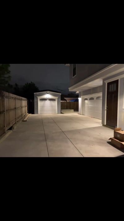New white garage door at night in Orange, at the end of a lit driveway beside a second door