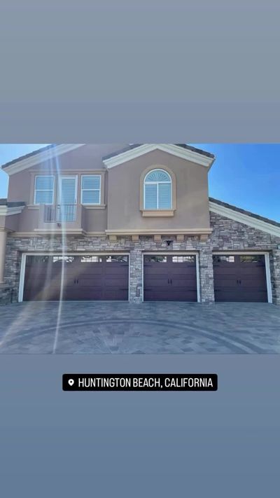 Three white garage doors with arched window detail on a single-story Huntington Beach home with palm trees
