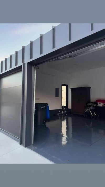 Charcoal flush-panel modern garage door standing open onto a finished garage with a glossy epoxy floor