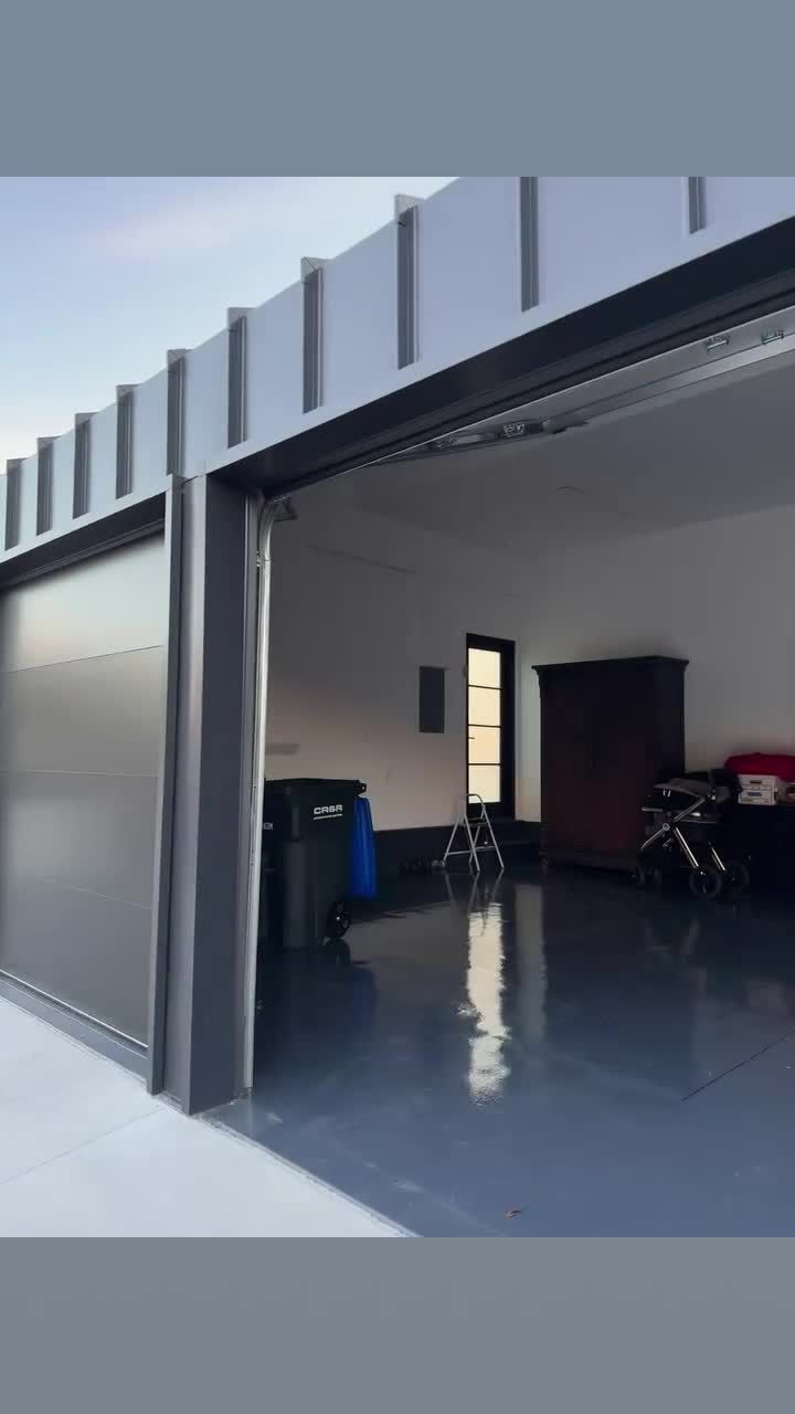 Charcoal flush-panel modern garage door standing open onto a finished garage with a glossy epoxy floor