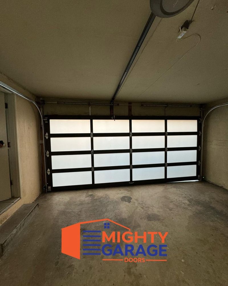 Full-view aluminum and glass garage door seen from inside an empty garage, daylight showing through the panels