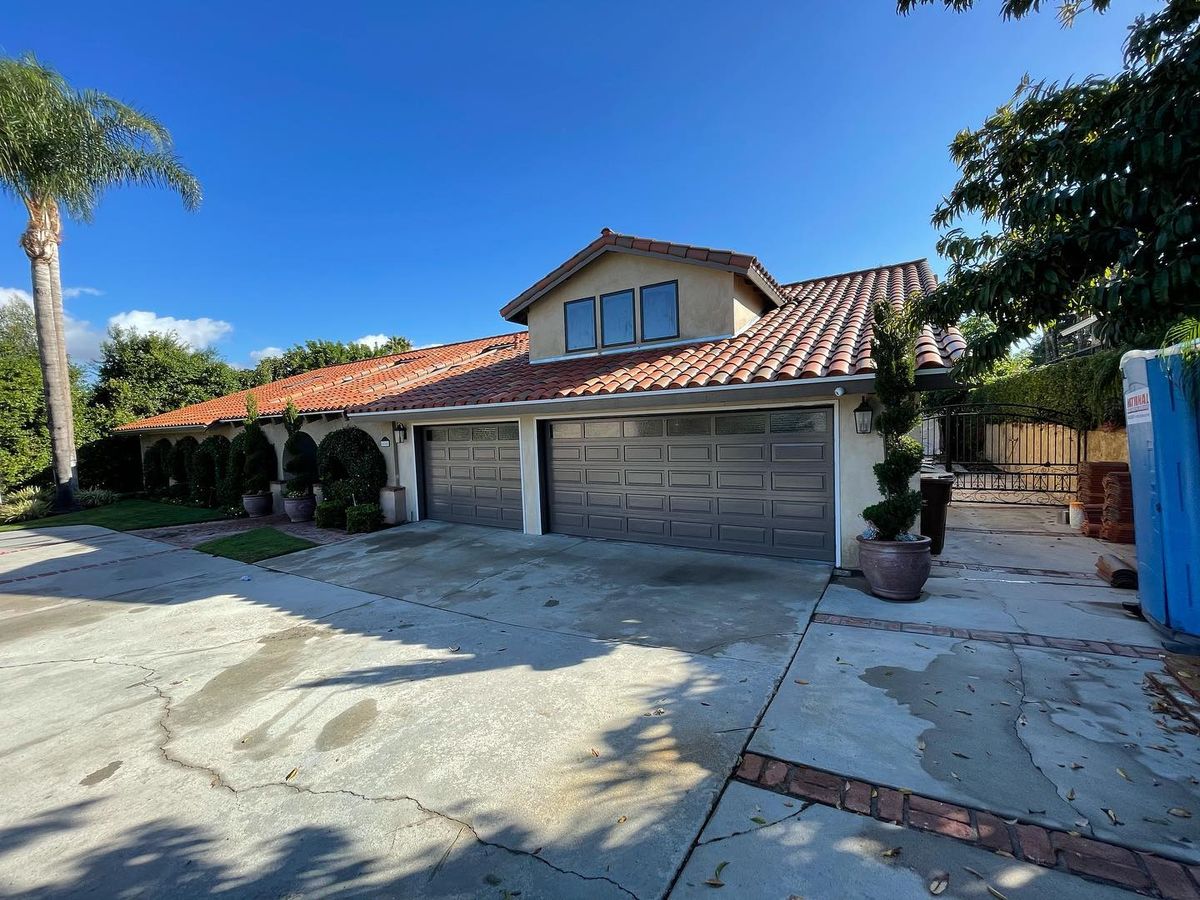 Dark brown garage doors on a single-story Yorba Linda home with a tile roof, palm tree and brick-trimmed driveway